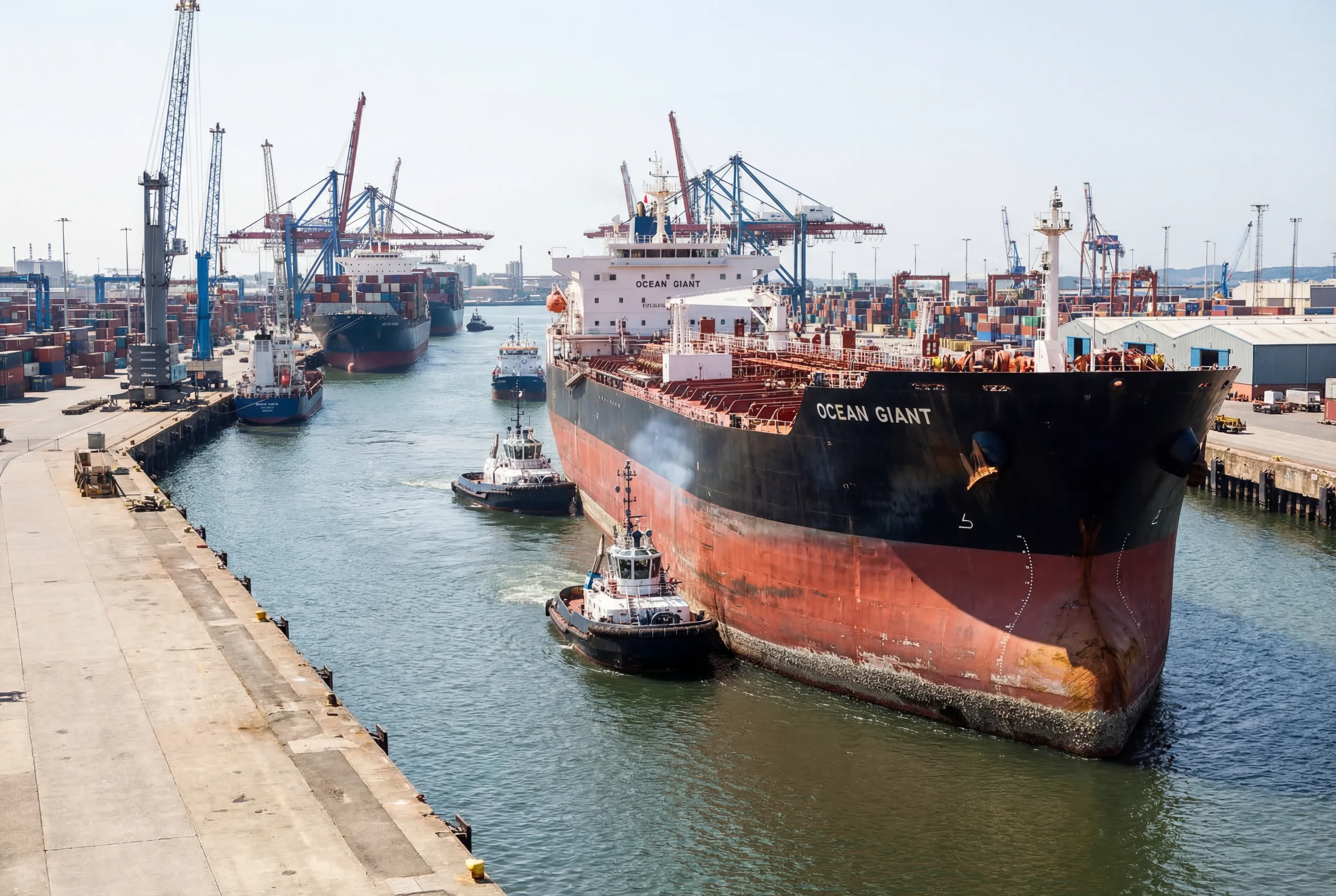 Bulk carrier Ocean Giant docking at a busy commercial port with tugboats, cranes, and container infrastructure